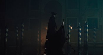 Movie still from “A Haunting in Venice” (2023), directed by Kenneth Branagh – A man in a black coat and a black hat riding on a boat; Wide shot, Low angle