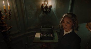 Movie still from “A Haunting in Venice” (2023), directed by Kenneth Branagh – An older woman standing in front of an old fashioned typewriter; Medium shot, High angle