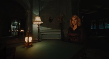 Movie still from “A Haunting in Venice” (2023), directed by Kenneth Branagh – A woman sitting at a table in a dark room; Medium shot, High angle