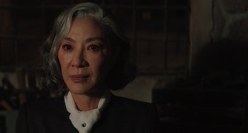 Movie still from “A Haunting in Venice” (2023), directed by Kenneth Branagh – An older asian woman with white hair looking at the camera; Close Up shot, Over the shoulder angle