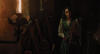 Movie still from “A Haunting in Venice” (2023), directed by Kenneth Branagh – A woman standing in front of a painting in a dark room; Medium shot, Over the shoulder angle