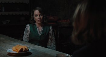 Movie still from “A Haunting in Venice” (2023), directed by Kenneth Branagh – A woman sitting at a table in front of a bowl of fruit; Medium shot, Over the shoulder angle
