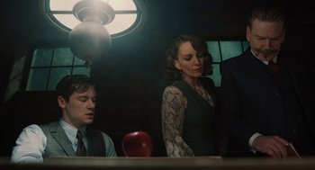 Movie still from “A Haunting in Venice” (2023), directed by Kenneth Branagh – A man and a woman sitting in front of a red apple on a table; Medium shot, Low angle