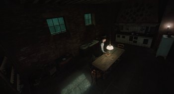 Movie still from “A Haunting in Venice” (2023), directed by Kenneth Branagh – A person sitting at a wooden table in a dark room; Extreme Wide shot, High angle