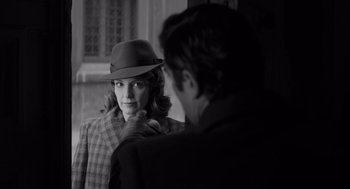 Movie still from “A Haunting in Venice” (2023), directed by Kenneth Branagh – A woman wearing a hat standing next to a man wearing a suit; Medium shot, Over the shoulder angle