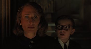 Movie still from “A Haunting in Venice” (2023), directed by Kenneth Branagh – A woman standing next to a young boy in glasses; Close Up shot, Low angle