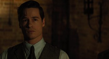 Movie still from “A Haunting in Venice” (2023), directed by Kenneth Branagh – A man wearing a suit and tie standing in front of a brick wall; Close Up shot, Over the shoulder angle