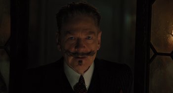 Movie still from “A Haunting in Venice” (2023), directed by Kenneth Branagh – A person wearing a suit and tie; Close Up shot, Low angle