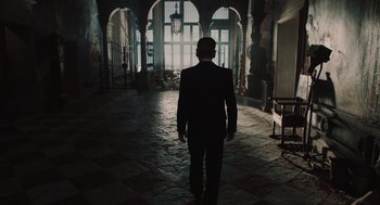 Movie still from “A Haunting in Venice” (2023), directed by Kenneth Branagh – A man in a black suit walking in an arched hallway; Wide shot, Low angle