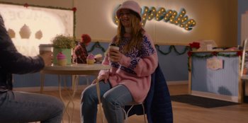 Movie still from “A Hollywood Christmas” (2022), directed by Alex Ranarivelo – A woman sitting at a table holding a cell phone; Medium shot, Over the shoulder angle