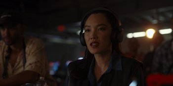 Movie still from “A Hollywood Christmas” (2022), directed by Alex Ranarivelo – A woman wearing headphones while standing in a room; Close Up shot, Over the shoulder angle