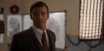 Movie still from “A Hollywood Christmas” (2022), directed by Alex Ranarivelo – A man in a suit and tie smiling for the camera; Close Up shot, Over the shoulder angle