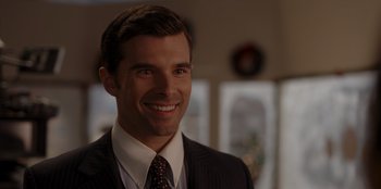 Movie still from “A Hollywood Christmas” (2022), directed by Alex Ranarivelo – A man wearing a suit and tie smiling for the camera; Close Up shot, Over the shoulder angle