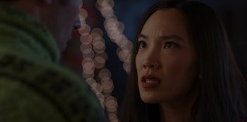 Movie still from “A Hollywood Christmas” (2022), directed by Alex Ranarivelo – A young woman looking at the camera while standing in front of a blurry background; Close Up shot, Over the shoulder angle