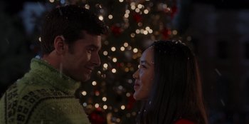 Movie still from “A Hollywood Christmas” (2022), directed by Alex Ranarivelo – A man and a woman looking at one another in front of a christmas tree; Close Up shot, Over the shoulder angle