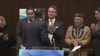 Two men in suits shaking hands in front of two other men