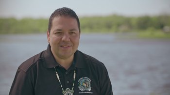 A man in a black shirt is standing in front of a body of water
