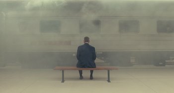 Movie still from “A Man Called Otto” (2022), directed by Marc Forster – A man sitting on top of a bench in front of a train; Wide shot, Low angle