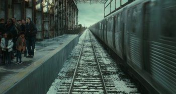 Movie still from “A Man Called Otto” (2022), directed by Marc Forster – A train traveling down the tracks next to a building; Extreme Wide shot, High angle