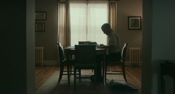 Movie still from “A Man Called Otto” (2022), directed by Marc Forster – A man sitting at a table in front of a laptop computer; Wide shot, Low angle