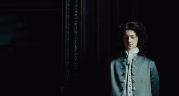 Movie still from “The Favourite” (2018), directed by Yorgos Lanthimos – A young man in a gray coat standing next to a wall; Medium shot, High angle
