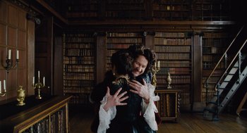 Movie still from “The Favourite” (2018), directed by Yorgos Lanthimos – Two people hugging in a library with a lot of bookshelves in the background; Medium shot, Over the shoulder angle