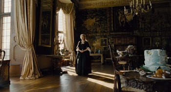 Movie still from “The Favourite” (2018), directed by Yorgos Lanthimos – A woman standing in a room with a lot of furniture; Wide shot, Low angle