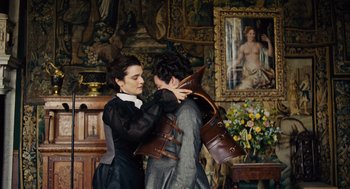 Movie still from “The Favourite” (2018), directed by Yorgos Lanthimos – A man and a woman are holding each other in front of a painting; Medium shot, Over the shoulder angle