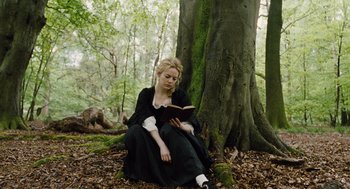 Movie still from “The Favourite” (2018), directed by Yorgos Lanthimos – A woman sitting in the woods reading a book; Medium shot, Low angle