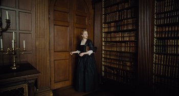 Movie still from “The Favourite” (2018), directed by Yorgos Lanthimos – A woman in a black dress standing in front of a book shelf; Wide shot, Low angle