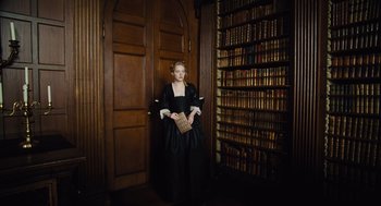 Movie still from “The Favourite” (2018), directed by Yorgos Lanthimos – A woman in a black dress standing in front of a book case; Medium shot, High angle