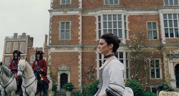 Movie still from “The Favourite” (2018), directed by Yorgos Lanthimos – A woman walking in front of a brick building; Medium shot, Low angle