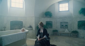 Movie still from “The Favourite” (2018), directed by Yorgos Lanthimos – A woman sitting in front of a baby in a bathtub; Wide shot, High angle