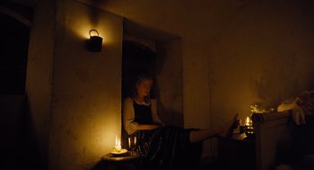 Movie still from “The Favourite” (2018), directed by Yorgos Lanthimos – A woman sitting on a window sill in a dark room; Wide shot, High angle