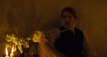 Movie still from “The Favourite” (2018), directed by Yorgos Lanthimos – A man in a black shirt holding a white cloth; Medium shot, Over the shoulder angle