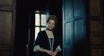 Movie still from “The Favourite” (2018), directed by Yorgos Lanthimos – A woman in a black dress standing next to a door; Medium shot, Low angle