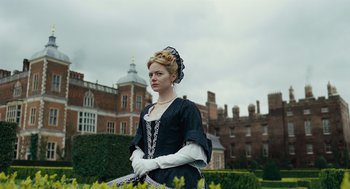 Movie still from “The Favourite” (2018), directed by Yorgos Lanthimos – A woman dressed in period clothing standing in front of a building; Medium shot, Low angle