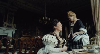 Movie still from “The Favourite” (2018), directed by Yorgos Lanthimos – Two women dressed in period clothing sitting at a dinner table; Medium shot, Low angle