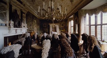 Movie still from “The Favourite” (2018), directed by Yorgos Lanthimos – A group of people sitting at a table in front of a chandelier; Wide shot, High angle
