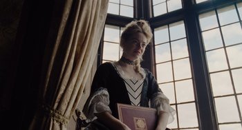 Movie still from “The Favourite” (2018), directed by Yorgos Lanthimos – A woman dressed in period clothing holding a book; Medium shot, Low angle