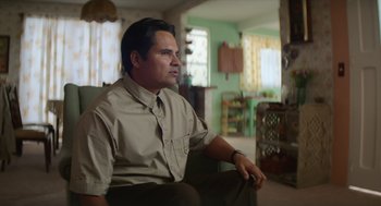 Movie still from “A Million Miles Away” (2023), directed by Alejandra Márquez Abella – A man sitting in a chair in a living room; Medium shot, Over the shoulder angle