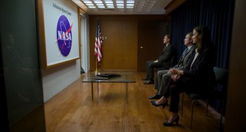 Movie still from “A Million Miles Away” (2023), directed by Alejandra Márquez Abella – Three men and a woman are sitting in front of a nasa sign; Wide shot, Over the shoulder angle