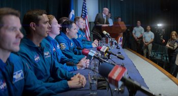 Movie still from “A Million Miles Away” (2023), directed by Alejandra Márquez Abella – A group of people sitting at a table with microphones; Medium shot, Over the shoulder angle