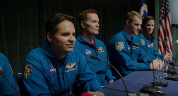 Movie still from “A Million Miles Away” (2023), directed by Alejandra Márquez Abella – Three men in blue space suits sitting at a table; Medium shot, Low angle