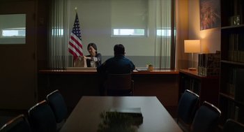Movie still from “A Million Miles Away” (2023), directed by Alejandra Márquez Abella – A man and a woman sitting in front of an american flag; Wide shot, Low angle