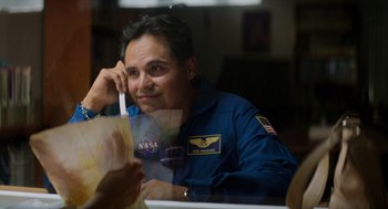 Movie still from “A Million Miles Away” (2023), directed by Alejandra Márquez Abella – A man sitting at a dining table with an airplane on his shirt; Medium shot, Over the shoulder angle