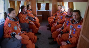 Movie still from “A Million Miles Away” (2023), directed by Alejandra Márquez Abella – A group of men in orange suits sitting in a room; Wide shot, High angle