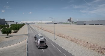 Movie still from “A Million Miles Away” (2023), directed by Alejandra Márquez Abella – An airstream traveling down a road near a cement field; Extreme Wide shot, High angle