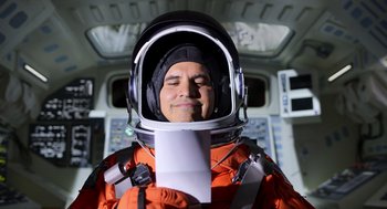 Movie still from “A Million Miles Away” (2023), directed by Alejandra Márquez Abella – A man in an orange space suit and a helmet; Medium shot, Overhead angle