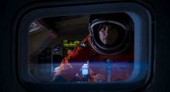 Movie still from “A Million Miles Away” (2023), directed by Alejandra Márquez Abella – A man in an orange space suit looking out of a window; Medium shot, Low angle